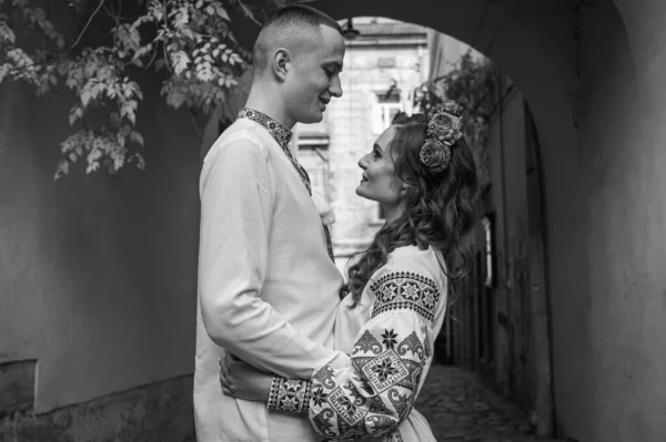 Black and white portrait. A happy young couple in love, a family walking through the old city of Lviv in Ukrainian embroidered dresses, holding hands. Young people hug in the old town of Lviv