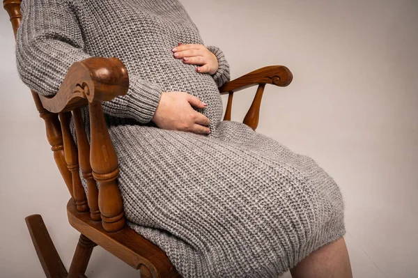Cropped image of beautiful pregnant woman in cradle chair, holding pregnant belly and loving life, light background, place for text. Close up view