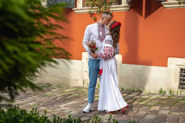 Emotional portrait of a happy young couple in love, a family hugging, holding hands in the city of Lviv in traditional Ukrainian shirts, holding hands. Young people hug in the old town of Lviv