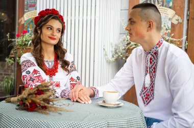 a young couple in love are sitting at a table in a cafe in Ukrainian traditional Ukrainian clothing, talking, emoting and drinking coffee. Couple in love.