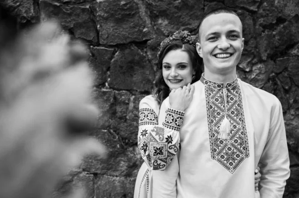 Black and white classic portrait of happy young couple in love, family hugging holding hands in Lviv city wearing traditional Ukrainian shirts. Young people hug in the old town of Lviv