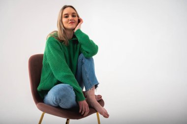 Full length photo of attractive chic businesswoman sitting commanding comfortable chair flirtatious mood empty space wearing jeans and green sweater on isolated white background, place for text