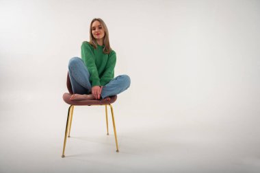 Full length photo of attractive chic businesswoman sitting commanding comfortable chair flirtatious mood empty space wearing jeans and green sweater on isolated white background, place for text