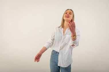 Portrait of a young, emotional, happy girl without makeup, smiling at the camera, gesturing with her hands, standing on a white background. Place for writing
