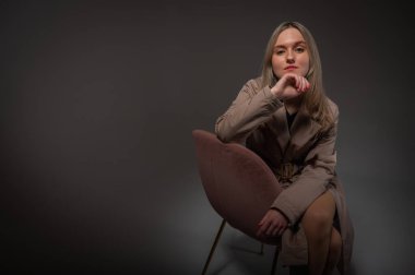 portrait of a young, emotional girl sitting on a chair in a flirtatious mood, gesturing with her hands, empty space, wearing a jacket, a dark cloak on an isolated white background, space for text
