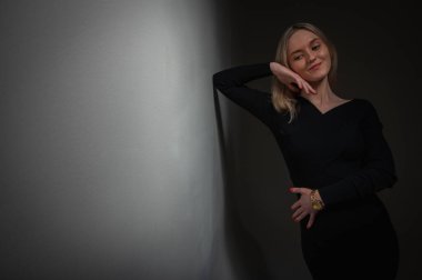 Portrait of an emotional chic girl standing in a flirtatious mood, gesturing with her hands, empty space, wearing a dark jacket on an isolated white background, place for text, beam of light, low key