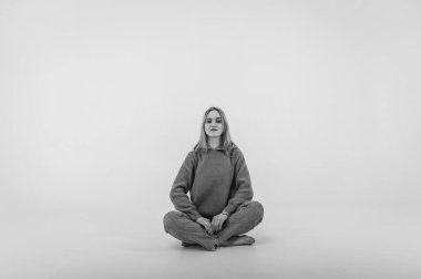 Portrait of a smiling young pretty European woman relaxing while sitting on the floor in jeans and a white shirt, isolated on white background. Place for writing