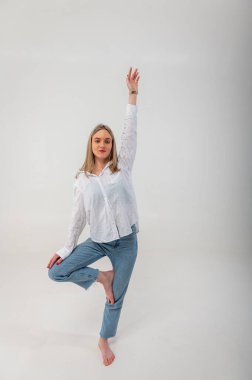 Sporty energetic active young girl stands on one leg meditating om sign, relaxes, rests. Light background with place for writing