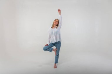 Sporty energetic active young girl stands on one leg meditating om sign, relaxes, rests. Light background with place for writing