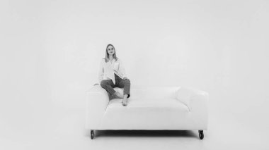 Siyah ve beyaz klasik, genç kız rahat, yumuşak, beyaz deri koltukta dinleniyor, sakin, halinden memnun kız kanepede uzanıyor. Işık arkaplanı üzerinde izole edilmiş, metin için yer