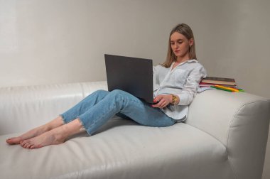 Kanepede dizüstü bilgisayarda oturan genç duygusal kız, arka planda izole edilmiş kız alışverişi ya da sosyal ağlarda sohbet, uzaktan çalışma. Yazmak için bir yer