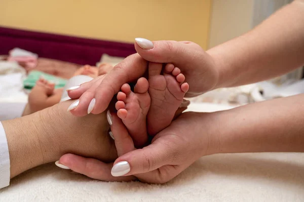 Baby feet in the hands of mother, father, older brother or sister, family. Feet of a tiny newborn close up. Little children\'s feet surrounded by the palms of the family. Parents and their child.