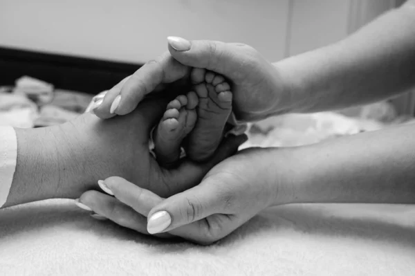 Baby feet in the hands of mother, father, older brother or sister, family. Feet of a tiny newborn close up. Little children\'s feet surrounded by the palms of the family. Parents and their child.