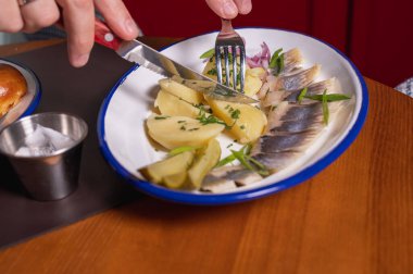 Bir adam restoranda, kafede yemek yiyor, soğanlı ringa turşusu kuruyor, masada çatal, ringa balığı tadıyor.