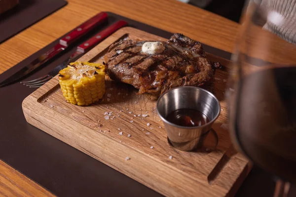 stock image a piece of juicy meat mid-roasting on a grill, on a wooden tray with corn. Delicious cuisine