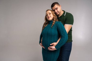 Hamile eşiyle birlikte beyaz duvar arkasında izole edilmiş mutlu genç bir adam görüntüsü. Aileyi büyütmek, çocuk sahibi olmak.