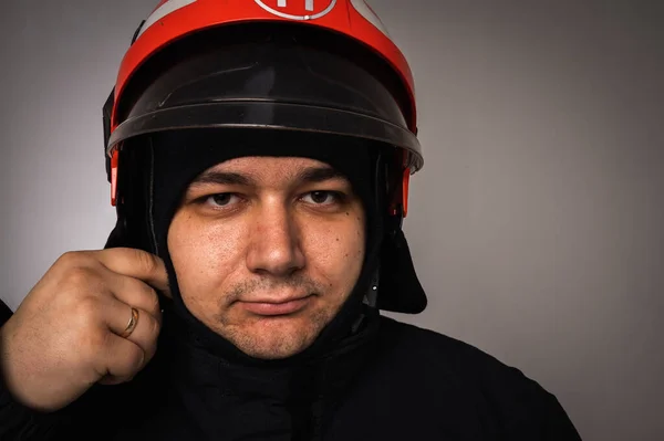 close-up portrait of a handsome firefighter in a helmet and gear, on a gray background and looking at the camera. Concept of saving lives, heroic profession, fire safety