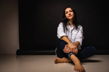 40 yaşlarında genç bir kızın iş portresi, sevimli, duygusal düşünceli, yerde oturuyor, karanlık bir arka plan, kapalı, yansıyan ışık, fotokopi uzayı ile çekiliyor.