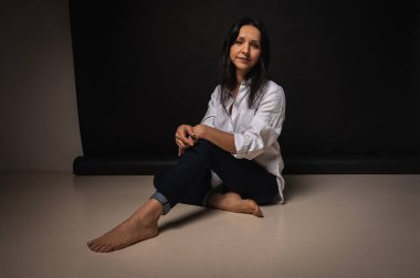 40 yaşlarında genç bir kızın iş portresi, sevimli, duygusal düşünceli, yerde oturuyor, karanlık bir arka plan, kapalı, yansıyan ışık, fotokopi uzayı ile çekiliyor.