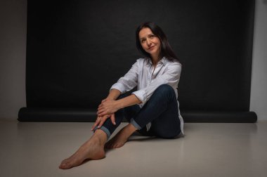 40 yaşlarında genç bir kızın iş portresi, sevimli, duygusal düşünceli, yerde oturuyor, karanlık bir arka plan, kapalı, yansıyan ışık, fotokopi uzayı ile çekiliyor.