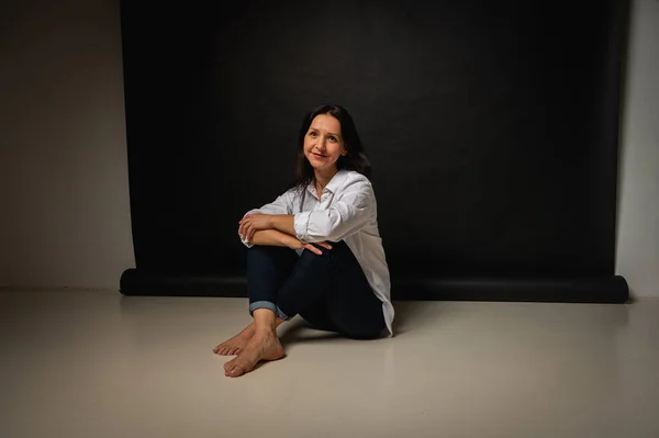 stock image business portrait of a young girl about 40 years old, cute, emotional thoughtful, sitting on the floor on a dark background, indoor, reflected light, shot with copy space