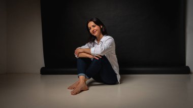 40 yaşlarında genç bir kızın iş portresi, sevimli, duygusal düşünceli, yerde oturuyor, karanlık bir arka plan, kapalı, yansıyan ışık, fotokopi uzayı ile çekiliyor.