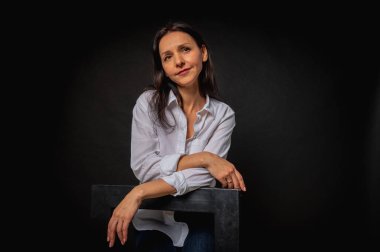 40 yaşlarında genç bir kızın iş portresi. Sevimli, duygusal düşünceli. Arka planda yüksek bir sandalyede oturuyor.