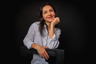 40 yaşlarında genç bir kızın iş portresi. Sevimli, duygusal düşünceli. Arka planda yüksek bir sandalyede oturuyor.