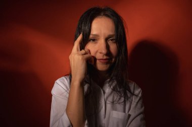 Yakın plan fotoğraf, ciddi, düşünceli, koyu turuncu arka planda bir kızın portresi, kendine güvenli ve dramatik görünüyor. Kadın portresi konsepti. Alçak tuş