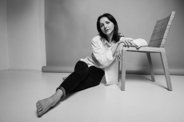 40 yaşlarında genç bir kızın siyah beyaz portresi, sevimli, duygusal düşünceli, yerde oturuyor, karanlık bir arka planda, kapalı alanda, yansıtılmış ışık, fotokopi uzayı ile çekiliyor.