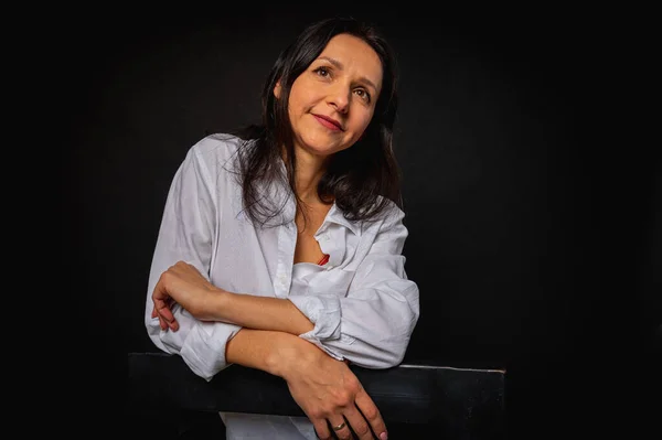 stock image business portrait of a young girl around 40 years old, cute, emotional thoughtful, sitting on a high chair on a dark background, studio shot with copy space