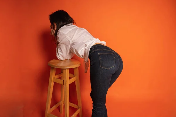 一个漂亮而严肃的女孩靠着椅子 背对着我们 背对着明亮的橙色背景 看起来自信而引人注目地笔直的特写照片 女性肖像画的概念 — 图库照片
