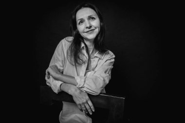 40 yaşlarında genç bir kızın siyah beyaz portresi, sevimli, duygusal düşünceli, yerde oturuyor, karanlık bir arka planda, kapalı alanda, yansıtılmış ışık, fotokopi uzayı ile çekiliyor.