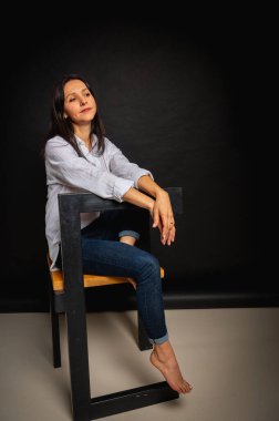 Sevimli ve baştan çıkarıcı esmer kadının uzun bir fotoğrafı. Pantolon giymiş, beyaz gömlekli, siyah arka planda izole bir kadın.