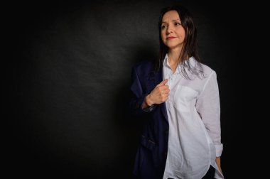 Genç ve güzel bir kızın iş portresini kaybetmek, duygusal düşünceli gülümseme, karanlık arka planda durmak, yan bakmak, beyaz gömlek ve kot pantolon, fotokopi ile çekilen stüdyo resmi.