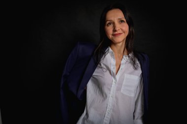 Genç ve güzel bir kızın iş portresini kaybetmek, duygusal düşünceli gülümseme, karanlık arka planda durmak, yan bakmak, beyaz gömlek ve kot pantolon, fotokopi ile çekilen stüdyo resmi.