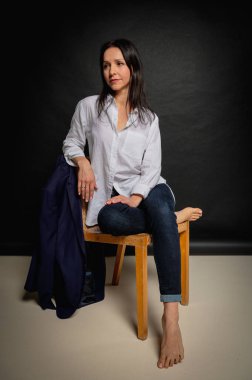 Karanlık bir sandalyede oturan ve ellerini yüzünün yakınında tutan bir kızın duygusal yakın plan portresi. Karanlık bir arka plan, yazmak için yer. El ve vücut hareketleri, portre 