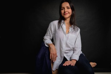 Karanlık bir sandalyede oturan ve ellerini yüzünün yakınında tutan bir kızın duygusal yakın plan portresi. Karanlık bir arka plan, yazmak için yer. El ve vücut hareketleri, portre 