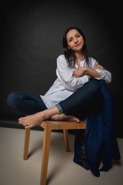 Karanlık bir sandalyede oturan ve ellerini yüzünün yakınında tutan bir kızın duygusal yakın plan portresi. Karanlık bir arka plan, yazmak için yer. El ve vücut hareketleri, portre 