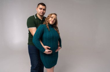 Hamile eşiyle birlikte beyaz duvar arkasında izole edilmiş mutlu genç bir adam görüntüsü. Bir aile kurmak, bir çocuk beklemek, genç bir aile, duygular.