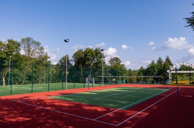 Parktaki bir spor sahasında yapay çimenler ve yeşil ağaçların arka planında gerilmiş bir ağ, güneşin sabah ışıklarıyla, şafakta