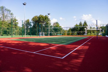 Parktaki bir spor sahasında yapay çimenler ve yeşil ağaçların arka planında gerilmiş bir ağ, güneşin sabah ışıklarıyla, şafakta