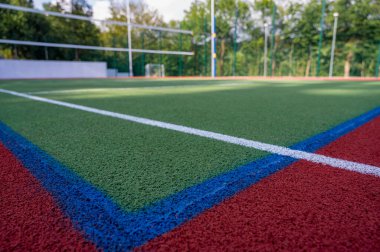 Parktaki bir spor sahasında yapay çimenler ve yeşil ağaçların arka planında gerilmiş bir ağ, güneşin sabah ışıklarıyla, şafakta