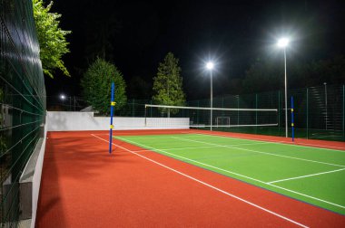 Sports volleyball field in the park with artificial grass of the stadium on the background of green trees. evening lighting with powerful lanterns, view from below clipart