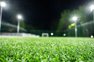 Parktaki spor sahasında yeşil ağaçların arkasında yapay çimen stadyumu var. Güçlü fenerlerle gece aydınlatması, aşağıdan manzara