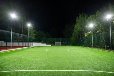 Parktaki spor sahasında yeşil ağaçların arkasında yapay çimen stadyumu var. Güçlü fenerlerle gece aydınlatması, aşağıdan manzara