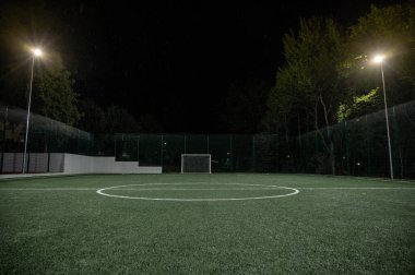 Parktaki spor sahasında yeşil ağaçların arkasında yapay çimen stadyumu var. Güçlü fenerlerle gece aydınlatması, aşağıdan manzara