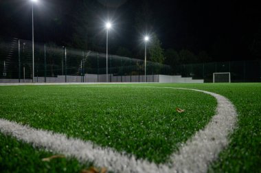 Parktaki spor sahasında yeşil ağaçların arkasında yapay çimen stadyumu var. Güçlü fenerlerle gece aydınlatması, aşağıdan manzara