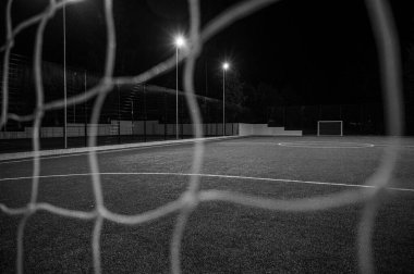 Siyah beyaz fotoğraf, yeşil ağaçların arka planında stadyumun yapay çimleriyle parkta akşam sporu sahası. Güçlü fenerlerle gece aydınlatması, aşağıdan manzara