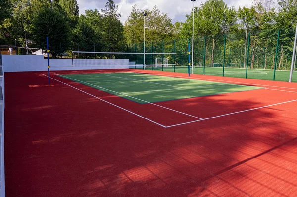 Parktaki bir spor sahasında yapay çimenler ve yeşil ağaçların arka planında gerilmiş bir ağ, güneşin sabah ışıklarıyla, şafakta